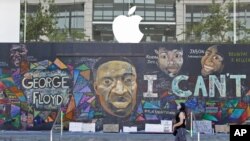 FILE - A pedestrian walks past a boarded-up Apple Store covered in street art in Portland, Ore., July 13, 2020. While most demonstrations in the city have been peaceful, nightly violent clashes between police and protesters have divided the city.