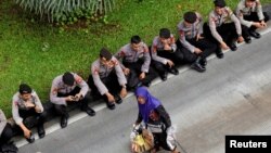 Para anggota Polri beristirahat di dekat Monas sementara seorang nenek penjaja makanan lewat di depan mereka pada aksi buruh memperingati "May Day" 1 Mei 2019 (foto: ilustrasi). 