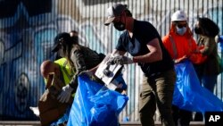 Gubernur California Gavin Newsom (tengah) ikut memunguti karton-karton bekas dari rel kereta api Union Pacific di Los Angeles, 20 Januari 2022. ( (AP/Ashley Landis)