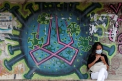 A woman sits in front of graffiti amidst the spread of coronavirus on a street in Brasilia, Brazil, March 11, 2021.
