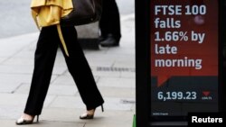 A woman passes an electronic sign showing the FTSE 100 index, in the City of London, July 3, 2013. 