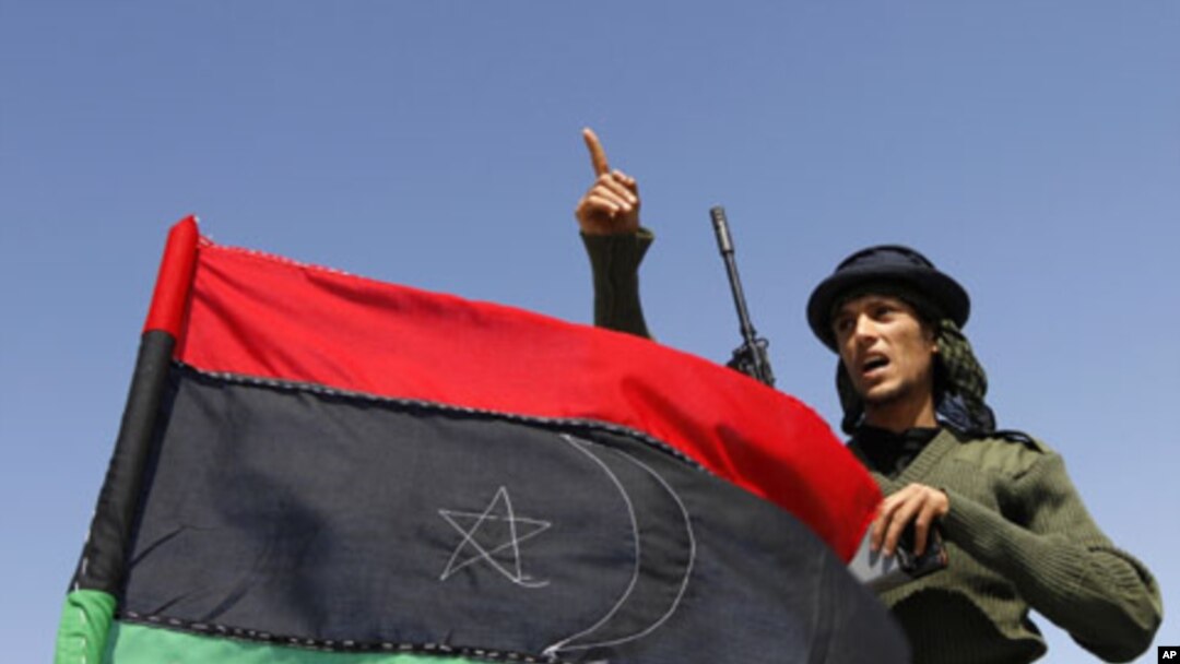 A rebel fighter gestures beside a Kingdom of Libya flag on a truck at a staging area to the east of Brega, April 4, 2011