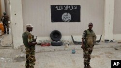 Des soldats nigérians se tiennent à un poste de contrôle devant un drapeau de Boko Haram la ville de Damasak, Nigeria, 18 mars 2015.