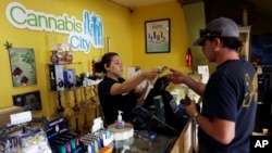 FILE - Jessica Mann, left, gives change to a customer following a recreational marijuana purchase at Cannabis City, in Seattle, July 7, 2016. 