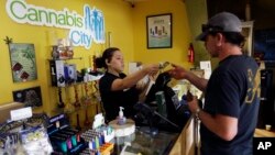 FILE - Jessica Mann, left, gives change to a customer following a recreational marijuana purchase at Cannabis City, in Seattle, July 7, 2016. Officials in states like Oregon where marijuana is legal are trying to curtail smuggling of pot to other states. Meanwhile, U.S. Attorney General Jeff Sessions is pushing for a more aggressive approach in these states, noting the drug is being diverted to other states.