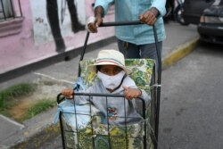 A child, wearing a protective face mask, eyes the camera as he is pushed in a grocery folding cart, in La Pastora neighborhood of Caracas, Venezuela, Aug. 22, 2020, amid the new coronavirus pandemic.