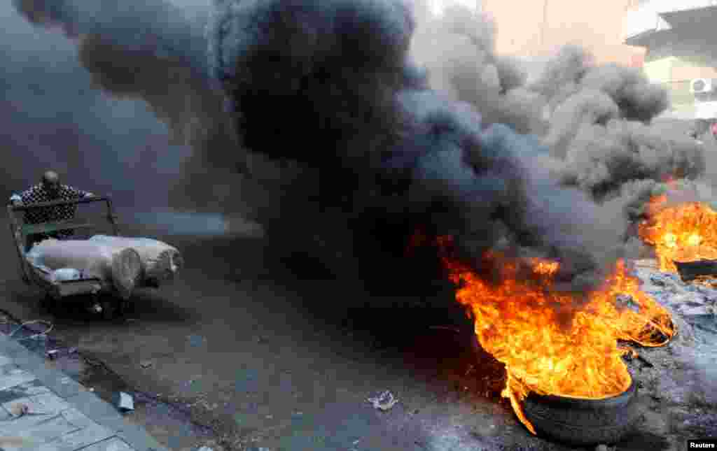 Iraqi demonstrators burn tires as they block the road during ongoing anti-government protests, in Baghda.
