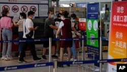 FILE - An airliner worker asks travelers to declare their health information after checking in at the international flight check in counter at the Beijing Capital International Airport in Beijing, Aug. 24, 2022. 