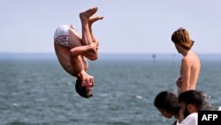 People jump off the Kerferd Road Pier as people cool off in the heatwave conditions at Melbourne's Albert Park Beach on November 22, 2024 (Photo by William WEST / AFP)