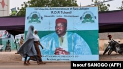 Des femmes passent devant une affiche de campagne de l'ancien président du Niger et candidat à la présidence, Mahamane Ousmane, le 18 février 2021 à Niamey.