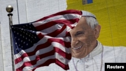 The U.S. flag flies in front of a mural of Pope Francis on the side of a building in midtown Manhattan in New York, Aug. 28, 2015.