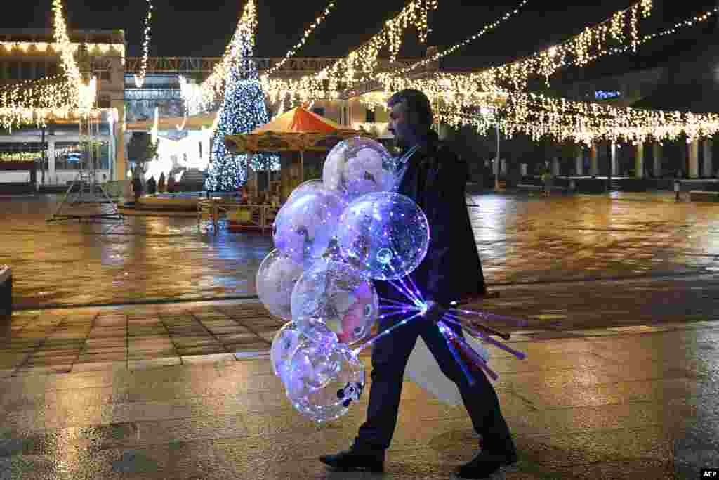 A man walks with balloons on an almost deserted Podgorica's central square, as New Year's Eve gatherings and celebrations have been restricted amid the COVID-19 pandemic, in Montenegro, Dec. 31, 2020.