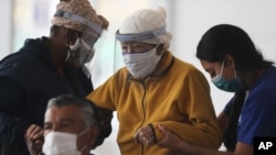 Una anciana es ayudada a subir a un cubículo para recibir una dosis de la vacuna Pfizer COVID-19, en el centro de convenciones convertido en sitio de vacunación, en Quito, Ecuador, el miércoles 31 de marzo de 2021.