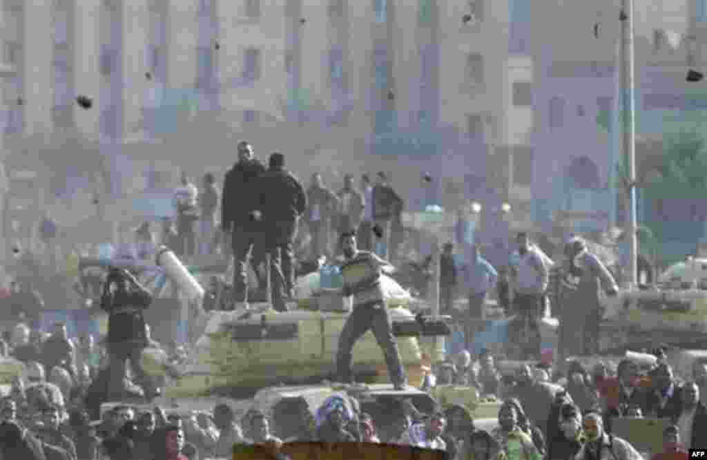 Stones fly through the air as supporters of President Hosni Mubarak, foreground , fight with anti-Mubarak protesters, rear, standing on army tanks in Cairo, Egypt, Wednesday, Feb.2, 2011. Several thousand supporters of Mubarak, including some riding hors