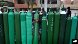 FILE - Edgar Barbaran exchanges a small, empty oxygen tank for a large one as he waits since the previous day for a refill shop to open in Callao, Peru, amid the COVID-19 pandemic on Jan. 25, 2021.