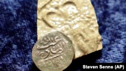 A 17th century Arabian silver coin made in 1693 in Yemen, rests against a piece of 17th century broken pottery featuring a likeness of Queen Mary. This ancient coin is important evidence to help solve a very old crime, March 11, 2021. (AP PHOTO/Steven Senne)