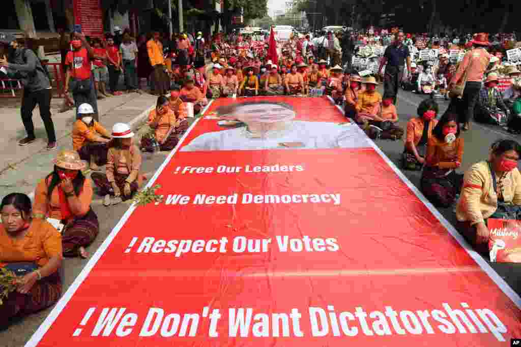 Protesters sit next to a giant banner with images of detained leader Aung San Suu Kyi during an anti-coup protest in Mandalay, Myanmar.