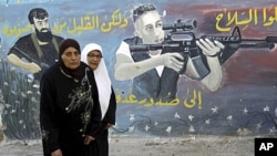 Palestinian women walk next to a mural of militants on the first day of Eid al-Fitr in the West Bank town of Jenin, August, 30, 2011.