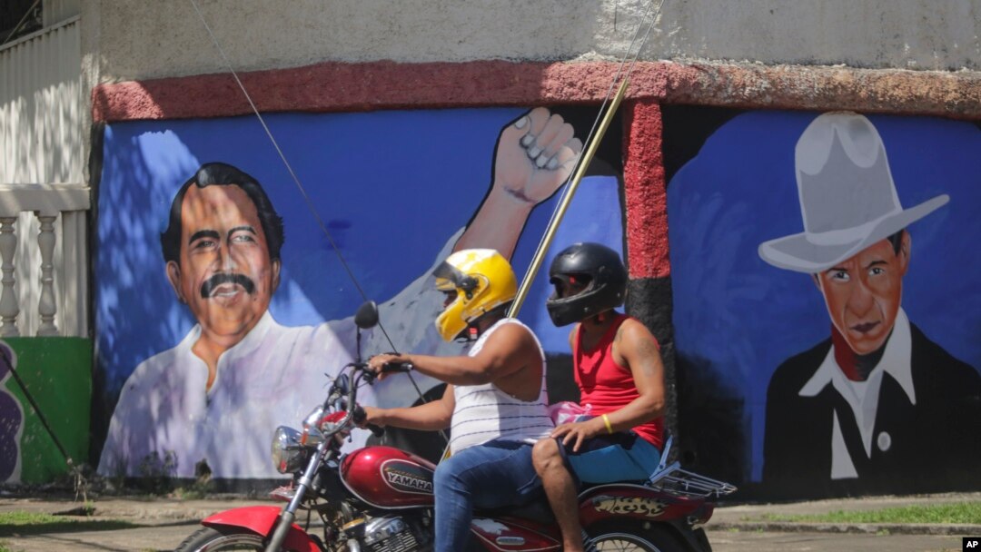 A motorcyclist rides past a mural of Nicaraguan President Daniel Ortega, left, and revolutionary hero Cesar Augusto Sandino during general elections in Managua, Nicaragua, Nov. 7, 2021.