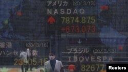 A woman wearing a protective face mask, following an outbreak of the coronavirus disease (COVID-19), is reflected in a screen displaying NASDAQ movements outside a brokerage in Tokyo, Japan March 16, 2020.