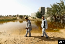 FILE - People walk next to a flooded plot of land in Libya's coastal city of Zliten February 13, 2024.