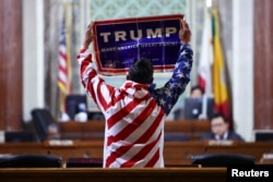 Seorang pengunjuk rasa membawa tanda TRUMP di Balai Kota Los Angeles saat Dewan Kota membahas peraturan "Kota Suaka", 19 November 2024. (Foto: Daniel Cole/Reuters)