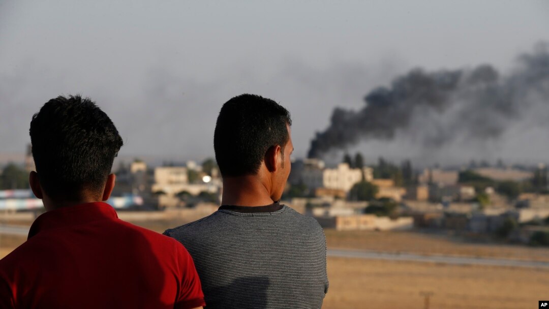 People standing on a rooftop in Akcakale, Sanliurfa province, southeastern Turkey, at the border with Syria, watch as in the background smoke billows from fires caused by Turkish bombardment in Tal Abyad, Syria, Sunday, Oct. 13, 2019. Turkey's…
