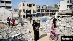 Una mujer palestina lleva a un niño mientras camina junto a los escombros de casas destruidas en ataques anteriores durante la ofensiva militar israelí, en medio del conflicto entre Israel y Hamas, en Khan Younis, en el sur de la Franja de Gaza, el 6 de noviembre de 2024. REUTERS