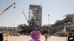 FILE - In this Sept. 20, 2019 file photo, taken during a trip organized by the Saudi information ministry, a man stands in front of the Khurais oil field in Khurais, Saudi Arabia, after it was hit during a Sept. 14 attack. 