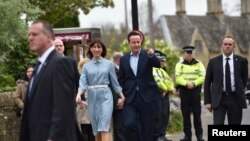 Perdana Menteri Inggris David Cameron tiba dengan istrinya Samantha untuk memberikan suara di Spelsbury, Inggris tengah (7/5). (Reuters/Toby Melville)