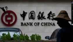 FILE - A man is silhouetted in front of a Bank of China's logo at its branch office in Beijing July 14, 2014.