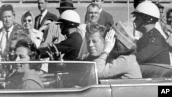 Presiden John F. Kennedy melambaikan tangan ke arah warga dari mobilnya dalam sebuah iring-iringan di Dallas, Texas, pada 22 November 1963. (Foto: AP/Jim Altgens)