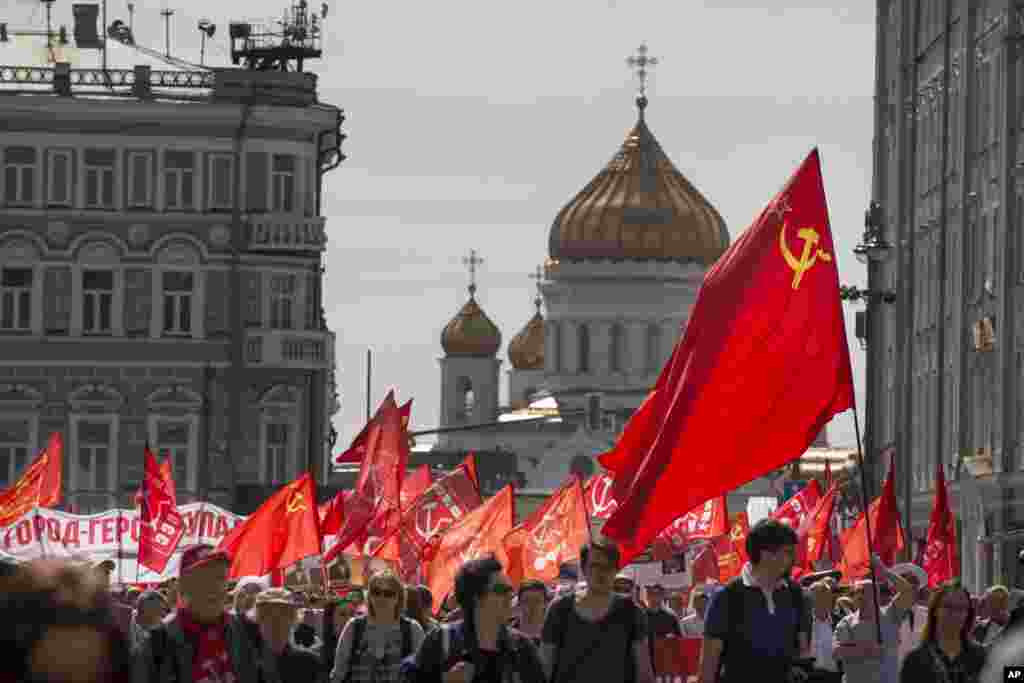 Orang-orang berpawai dengan membawa bendera merah dengan latar belakang Katedral Kristus Juru Selamat pada demo partai komunis untuk memperingati Hari Buruh di Moskow, Rusia, Senin, 1 Mei 2017.