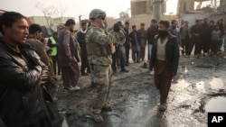 A U.S. soldier, center, takes a photo at the site of a suicide car bomb attack near the headquarters of the European Union police training mission in Kabul, Afghanistan, Jan. 5, 2015. 