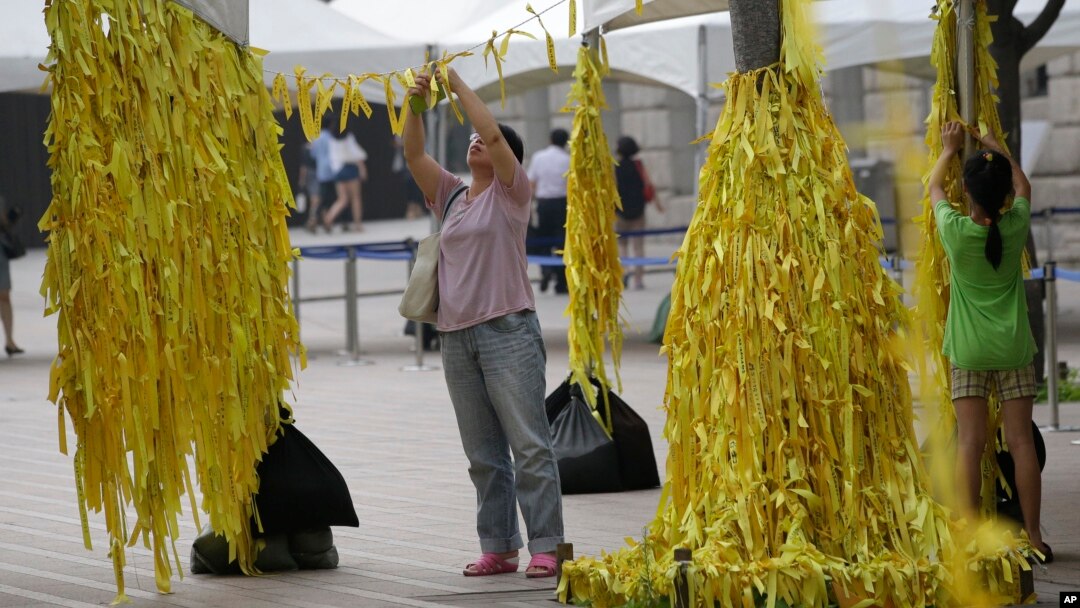 A mother and her daughter tie yellow ribbons with messages for missing passengers and victims aboard the sunken ferry Sewol in the water off the southern coast, at a group memorial altar in Seoul, South Korea, July 28, 2014. 