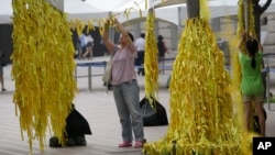 A mother and her daughter tie yellow ribbons with messages for missing passengers and victims aboard the sunken ferry Sewol in the water off the southern coast, at a group memorial altar in Seoul, South Korea, July 28, 2014. 