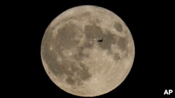 FILE - A plane passes in front of the moon, Aug. 30, 2023, in Chicago. Scientists have confirmed a cave on the moon and suspect there are hundreds more that could house future astronauts. (AP Photo/Kiichiro Sato, file)