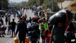 Migrants carry their belongings as they flee a road leading from Moria to the capital of Mytilene, on the northeastern island of Lesbos, Greece, Sept. 17, 2020. 