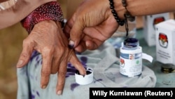 Seorang petugas pemilu membantu seorang perempuan lanjut usia untuk menandai jarinya dengan tinta setelah memberikan suaranya pada Pilkada di Tangerang, Banten, 27 Juni 2018. (Foto: REUTERS/Willy Kurniawan)