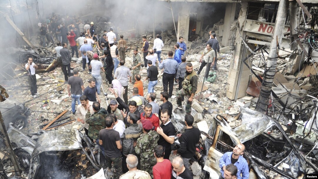 A crowd gathers in front of a building and car damaged after a bomb explosion in the Mezzeh 86 area in Damascus, in this handout photograph released by Syria's national news agency SANA, November 5, 2012. 