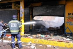 FILE - A shopkeeper watches as a fireman douses down a burned and damaged property after overnight unrest and looting in Alexandra township, Johannesburg, South Africa, Sept. 3, 2019.