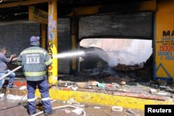 FILE - A shopkeeper watches as a fireman douses down a burned and damaged property after overnight unrest and looting in Alexandra township, Johannesburg, South Africa, Sept. 3, 2019.