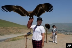 A vendor holds up an eagle as the waits for tourists to take photos with near the Terejl National Park outside Ulaanbaatar, Mongolia on July 3, 2024. (AP Photo/Ng Han Guan)