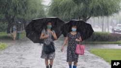 Women walk with umbrellas during torrential rains, Aug. 5, 2020, in Pyongyang. North Korea says torrential rains have lashed the country, prompting outside worries about possible severe damages in the impoverished country. 