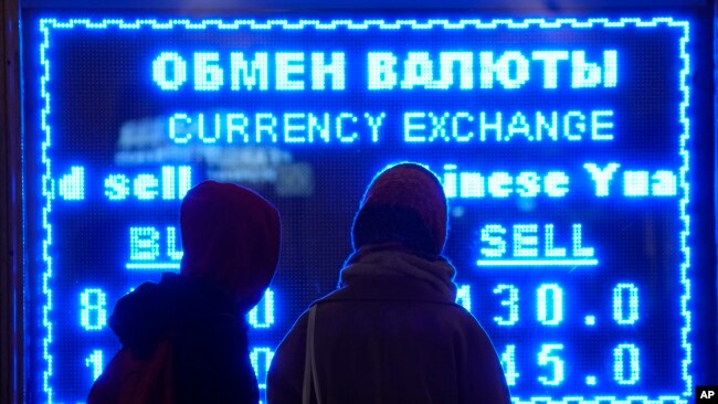 FILE - Women look at a screen showing the exchange rate at a money exchange office in St. Petersburg, Russia on March 1, 2022. (AP Photo/Dmitri Lovetsky, File)