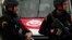 FILE - A Tunisian national flag is seen on a police vehicle as policemen stand guard following an attack by gunmen in Tunis, Tunisia, March 20, 2015.