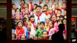 FILE - A visitor walks past a photo, Sept. 28, 2017, of Chinese President Xi Jinping surrounded by children at an exhibition highlighting five years of progress under Xi's leadership in Beijing. The birthrate in China fell in 2017 despite the easing of fa