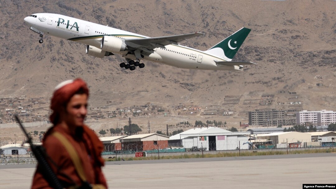 FILE - A Taliban fighter stands guard as a Pakistan International Airlines plane, the first commercial international flight to land after the Taliban retook power, takes off at the airport in Kabul on Sept. 13, 2021.