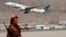 FILE - A Taliban fighter stands guard as a Pakistan International Airlines plane, the first commercial international flight to land since the Taliban retook power, takes off at the airport in Kabul on Sept. 13, 2021.