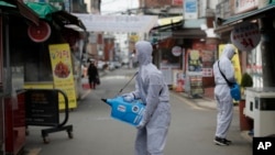 Workers wearing a protective suit spray disinfectant as a precaution against the COVID-19 at a market in Seoul, South Korea, Wednesday, Feb. 26, 2020.